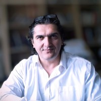 Headshot of Simon Patkovic in a white shirt with glasses on top of his head